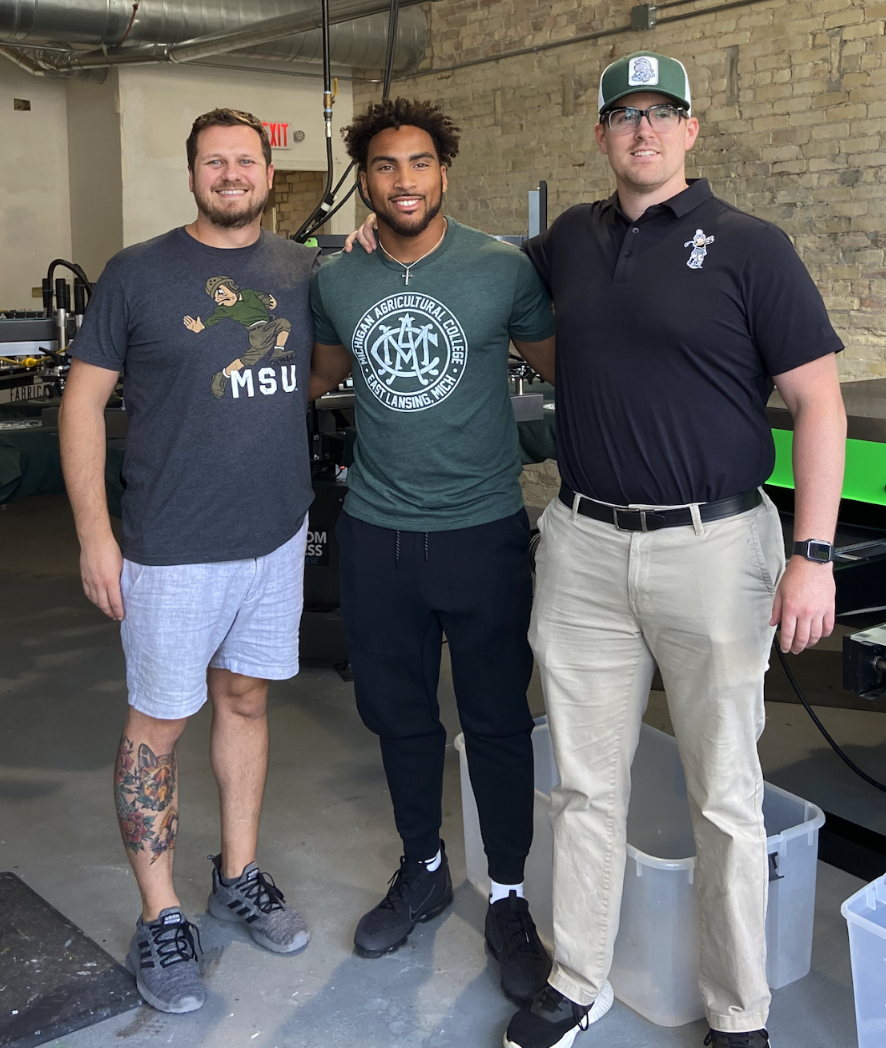 Group of guys wearing Michigan State Gear with MAC MSU Logo on Green t-shirt standing in the Nudge Printing shop