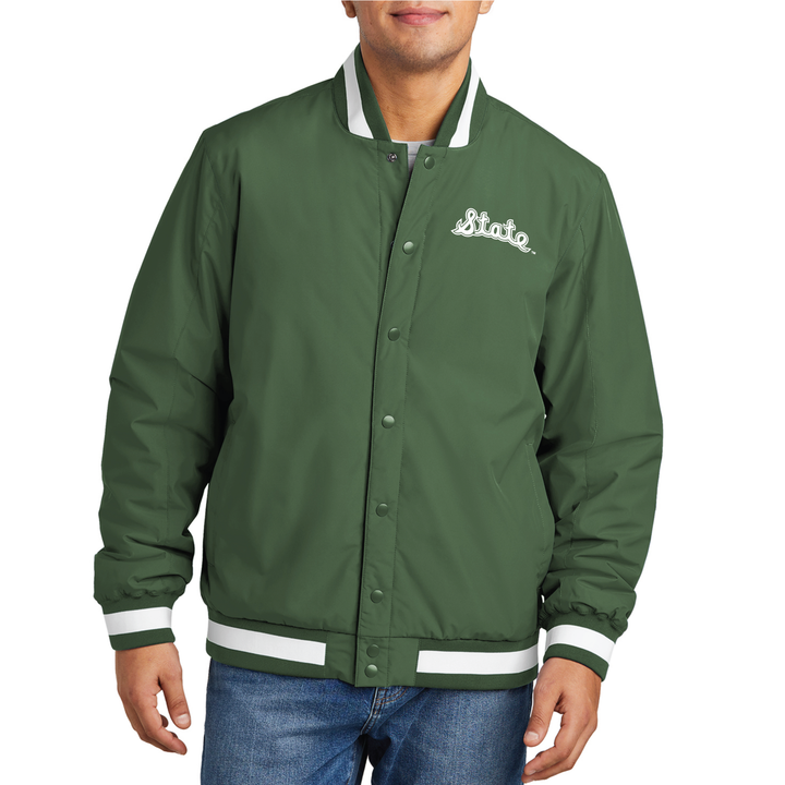 Male model wearing a green Michigan State varsity jacket with the cursive State Script logo embroidered in white thread on the left chest